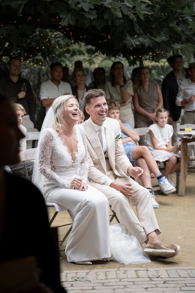 Marlou en Freek lachen tijdens de ceremonie op Domaine d’Heerstaayen, omringd door hun gasten